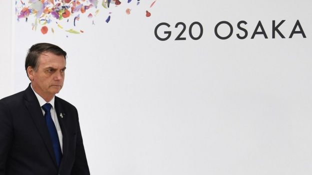O presidente Jair Bolsonaro próximo a painel em que se lê "G20 Osaka"