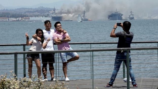 Люди фотографируются на фоне горящего судна