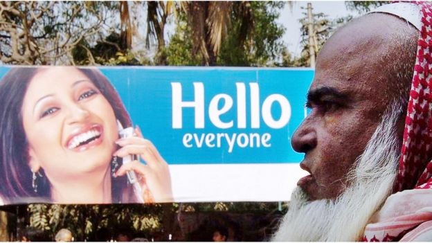 বাংলাদেশের ঢাকায় মোবাইল ফোনের বিজ্ঞাপনের পাশ দিয়ে একজন বৃদ্ধ হেঁটে যাচ্ছেন।