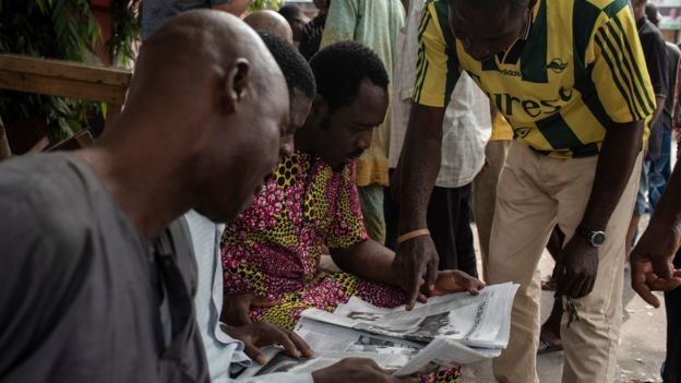 Nigerian men examine a newspaper after the postponement