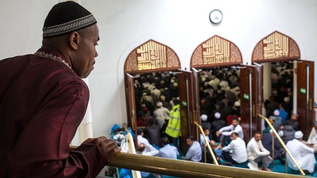 man looking from balcony at praying people in mosque