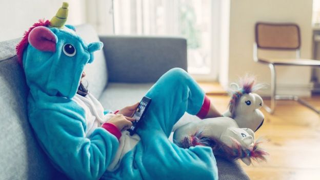 Fille vêtue d'un body de licorne, assise sur le canapé, utilisant une tablette.