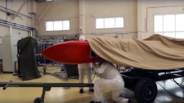 Homens trabalham ao redor de míssil vermelho russo coberto por uma lona