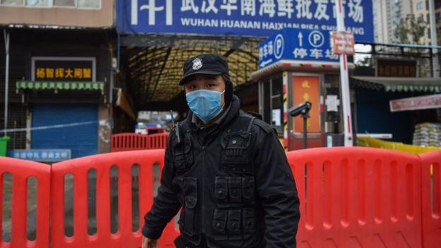 Policía usando máscara en frente de la entrada al mercado de Wuhan.