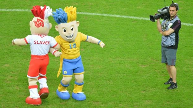A cameraman stands next Euro 2012 mascots, Polish Slavek (L) and Ukrainian Slavko