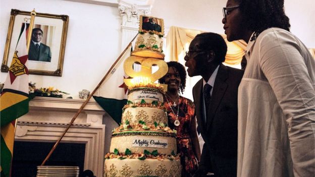 Zimbabwe President Robert Mugabe (C), flanked by his wife Grace Mugabe (L) and daughter Bona (R), blows candles on his cake during a suprise party hosted by the office of the President and Cabinet at State House in Harare, on February 22, 2016 to celebrate his 92nd birthday.