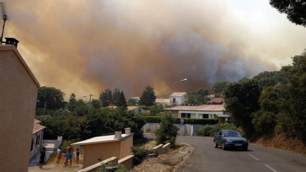 People stand outside a house as a fire burns Ortale di Biguglia, Corsica. Photo: 25 July 2017
