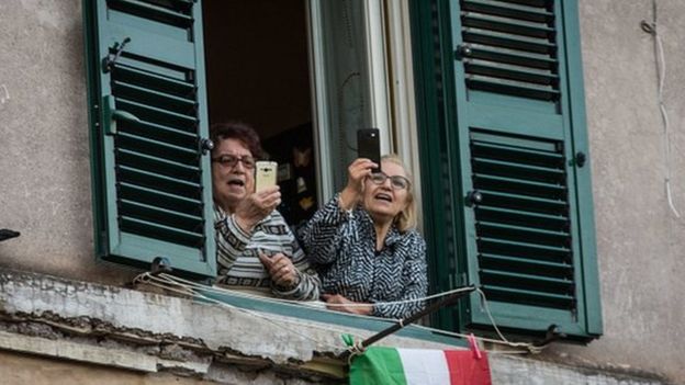 Dos mujeres con sus teléfonos en las manos mientras cantan en el balcón.