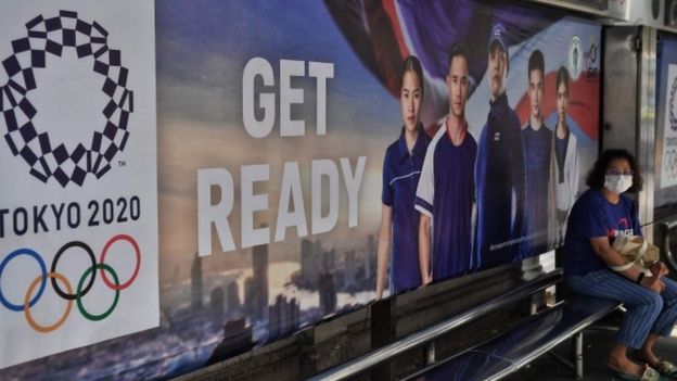 Woman wearing a mask at a bus stop with Tokyo 2020 advertising