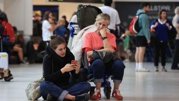 Passengers at Belfast International Airport sit on the airport floor and wait for flight news
