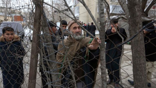 Bystanders with grim expressions watch the aftermath of a suicide attack on the Supreme Court in Kabul, Afghanistan, Tuesday, Feb. 7, 2017