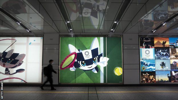 A commuter in a face mask walks in front of a poster of the 2020 Olympics mascot in Tokyo