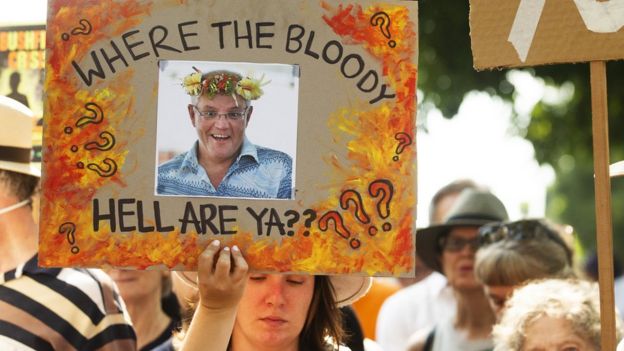 A protester in Sydney holds up a sign outside the Prime Minister's home showing a picture of Scott Morrison and a message: "Where the Bloody Hell Are Ya?"