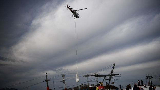 People look at a helicopter carrying snow near Luchon in the French Pyrenees