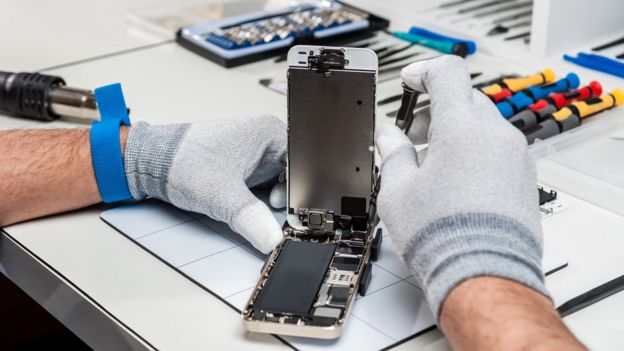 Two hands repairing a cell phone in a workshop.