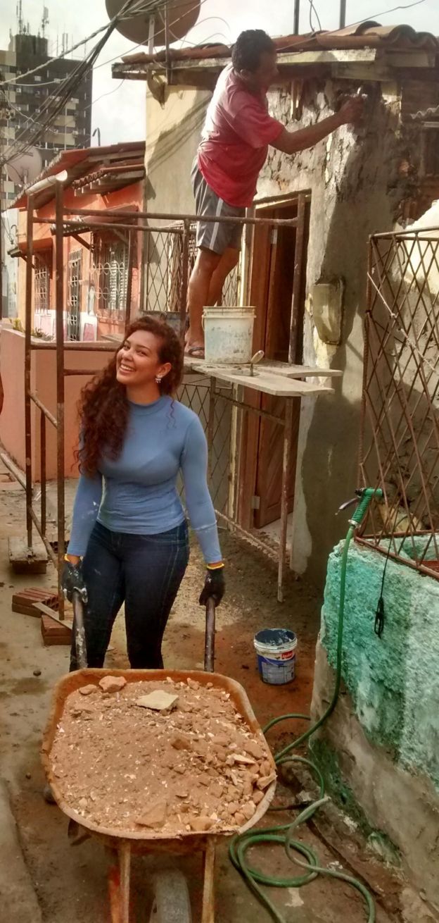 Imagem mostra Fernanda Silmara Silva dos Santos com carrinho de mão, próxima a pedreiro realizando obra