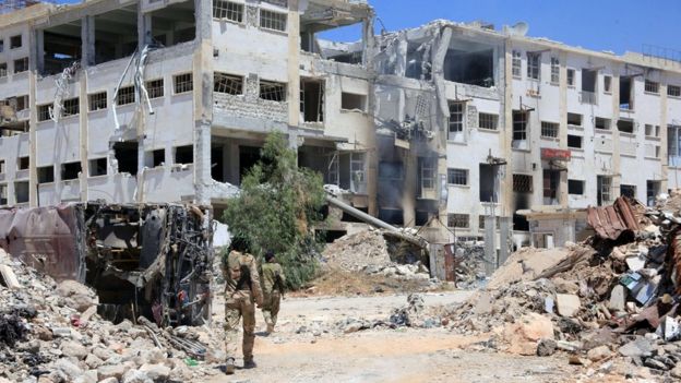 Forces loyal to President Bashar al-Assad walk past ruined buildings in the Castello road in Aleppo, Syria