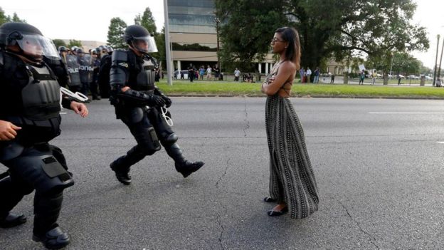 Una joven se mantiene de pie mientras funcionarios antimotines se le acercan