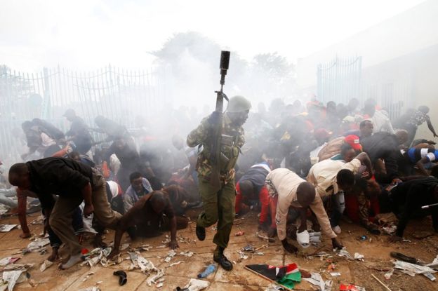 People fall as police fire tear gas to try control a crowd trying to force their way into a stadium to attend the inauguration of President Uhuru Kenyatta in Nairobi, Kenya, 28 November