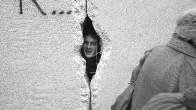 رجل ينظر من خلال ثقب في سور برلين