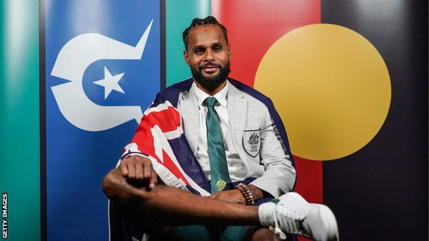 Australia's Olympic flag bearer Patty Mills posses in front of the Torres Strait and Aboriginal flags