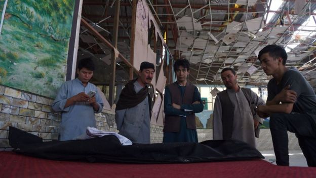 Men are inspecting the body of a victim wrapped in cloth