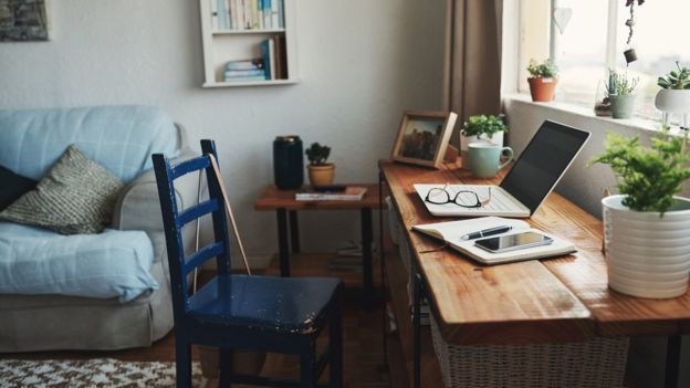 Sala de uma casa com computador, caderno, celular, caneta e óculos