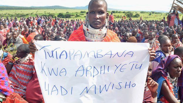 A Maasai woman holds a sign that reads in Swahili: "We will fight for our land until the end"