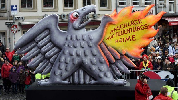 A carnival float, depicting the German federal eagle getting frightened as one of its wings burns due to attacks on refugee shelters.