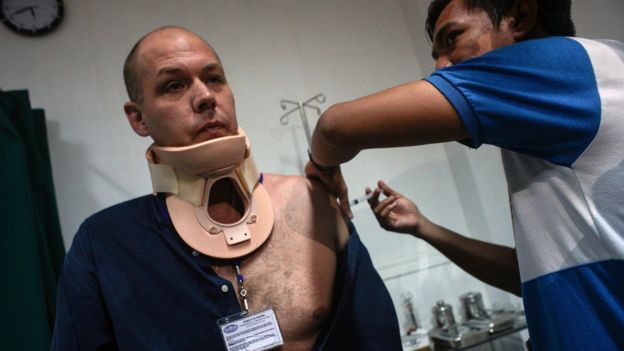 Adam Harvey in a neckbrace, being attended to by medical staff in a hospital