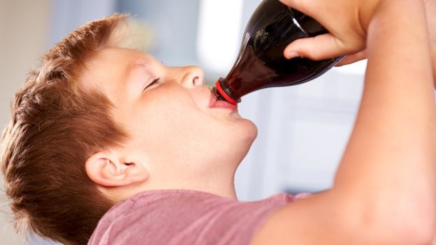 Niño de unos 8 años bebiendo un refresco de cola.