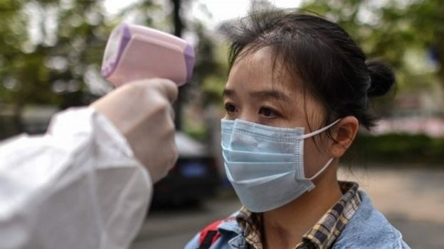 A man wearing a protective suit checks a woman's temperature next to a residential area in Wuhan, in China"s central Hubei province on April 7, 2020.