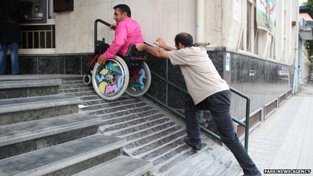 Pushing a man in a wheelchair up a ramp