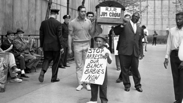 Demonstrators carry a mock coffin labeled "RIP Jim Crow," while a little boy parades with a sign saying "Stop arresting our black babies now," in front of the United Nations.