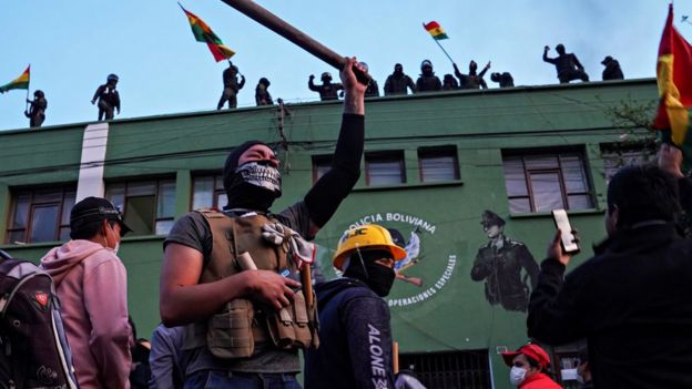 Opponents of Bolivia's President Evo Morales react as police officers stand on the roof of their headquarters, in Cochabamba, Bolivia