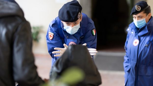 Mulher com roupa da cruz vermelha e máscara no rosto atende uma criança cujo rosto não é visível durante ação dos voluntários da Cruz Vermelha em Florença, na Itália