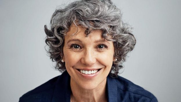 Mujer madura con rulos canosos y sonriendo.