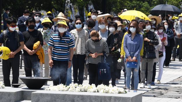 Dezenas de pessoas usando máscara durante cerimônia em cemitério