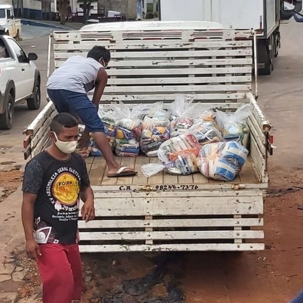 Dois homens em volta de caminhão com cestas básicas