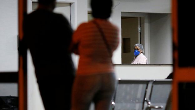 Enfermeira com máscara e vulto de duas pessoas dentro de sala de hospital em Brasília