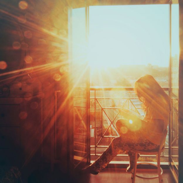 Una mujer sentada en un balcón con el Sol brillando fuertemente