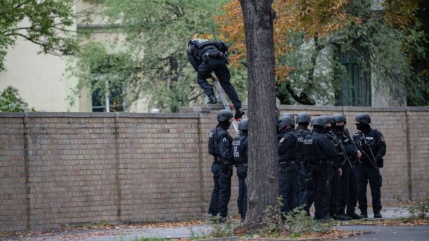 Police climb over a wall into a Jewish cemetery