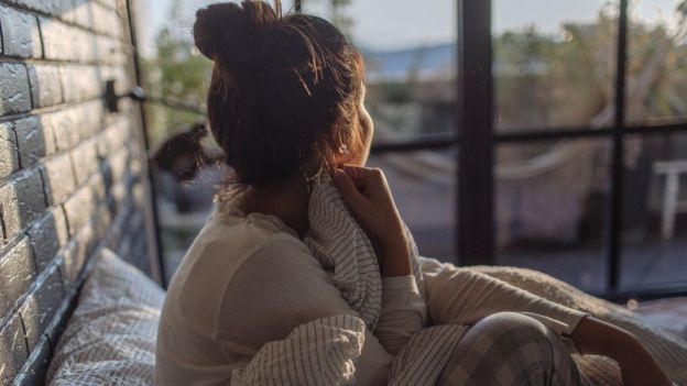 Una mujer sola en una habitación, mirando por la ventana.