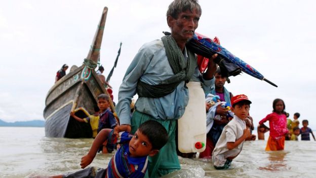 A Rohingya refugee man pulls a child as they walk to the shore after crossing the Bangladesh-Myanmar border by boat through the Bay of Bengal in Shah Porir Dwip, Bangladesh, 10 September 2017