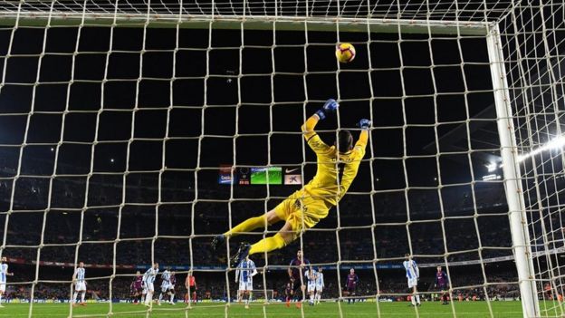 Goleiro salta para pegar bola em partida em estádio de futebol