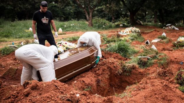Cemitério em São Paulo, com coveiro enterrando um caixão, observador por um parente homem