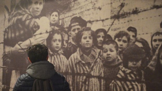 Hombre camina frente a una foto ampliada de prisioneros en un campo de concentraciÃ³n.