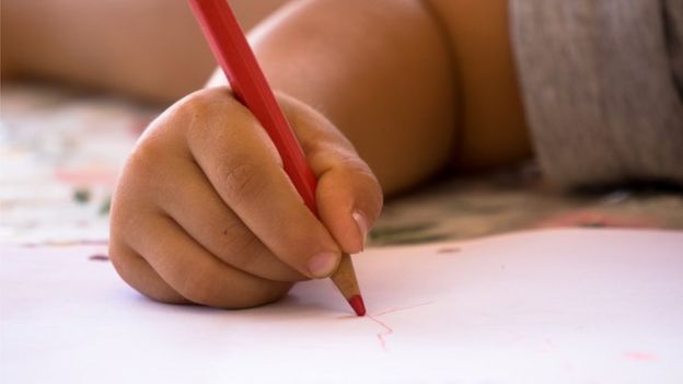 Un niño haciendo garabatos en un papel con un creyón rojo