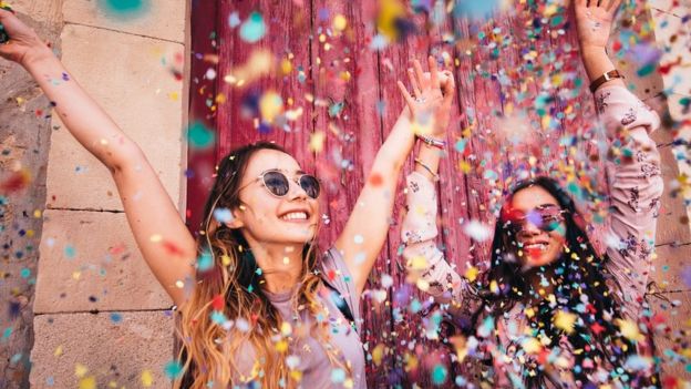 Cheerful female teenage best friends partying by throwing confetti in city streets