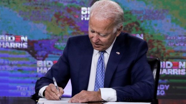 Biden sentado assinando documento